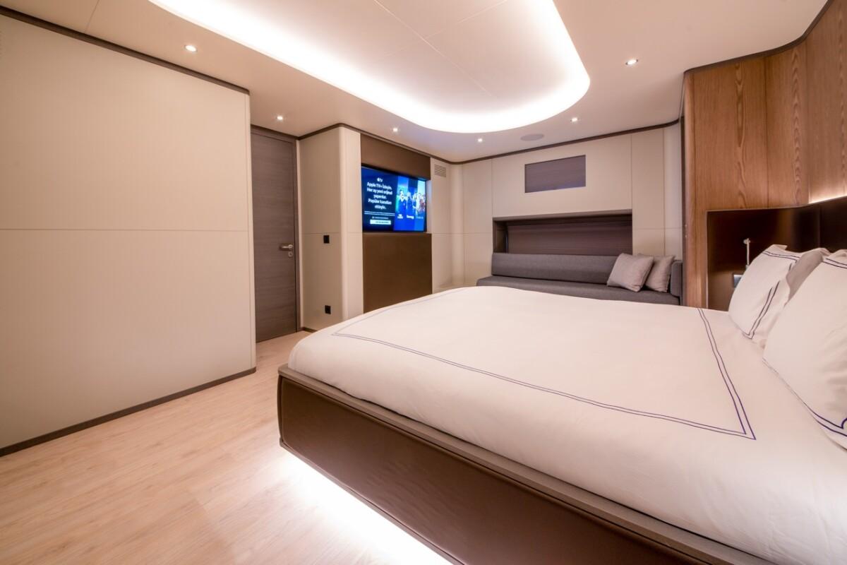 Modern yacht cabin featuring double bed with white linens and integrated entertainment system