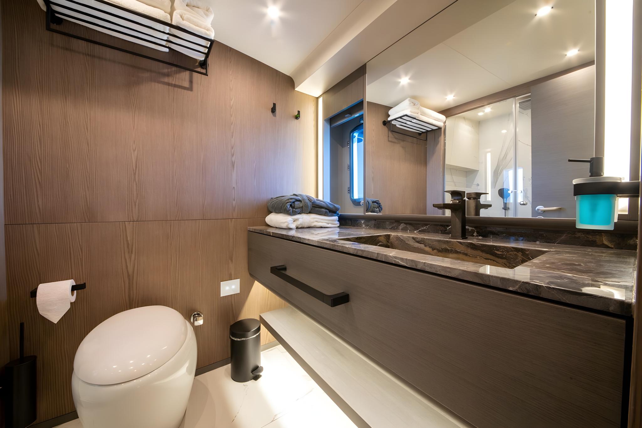 luxury yacht bathroom featuring dark marble vanity countertop, vessel sink, wall-mounted toilet, and wood paneling