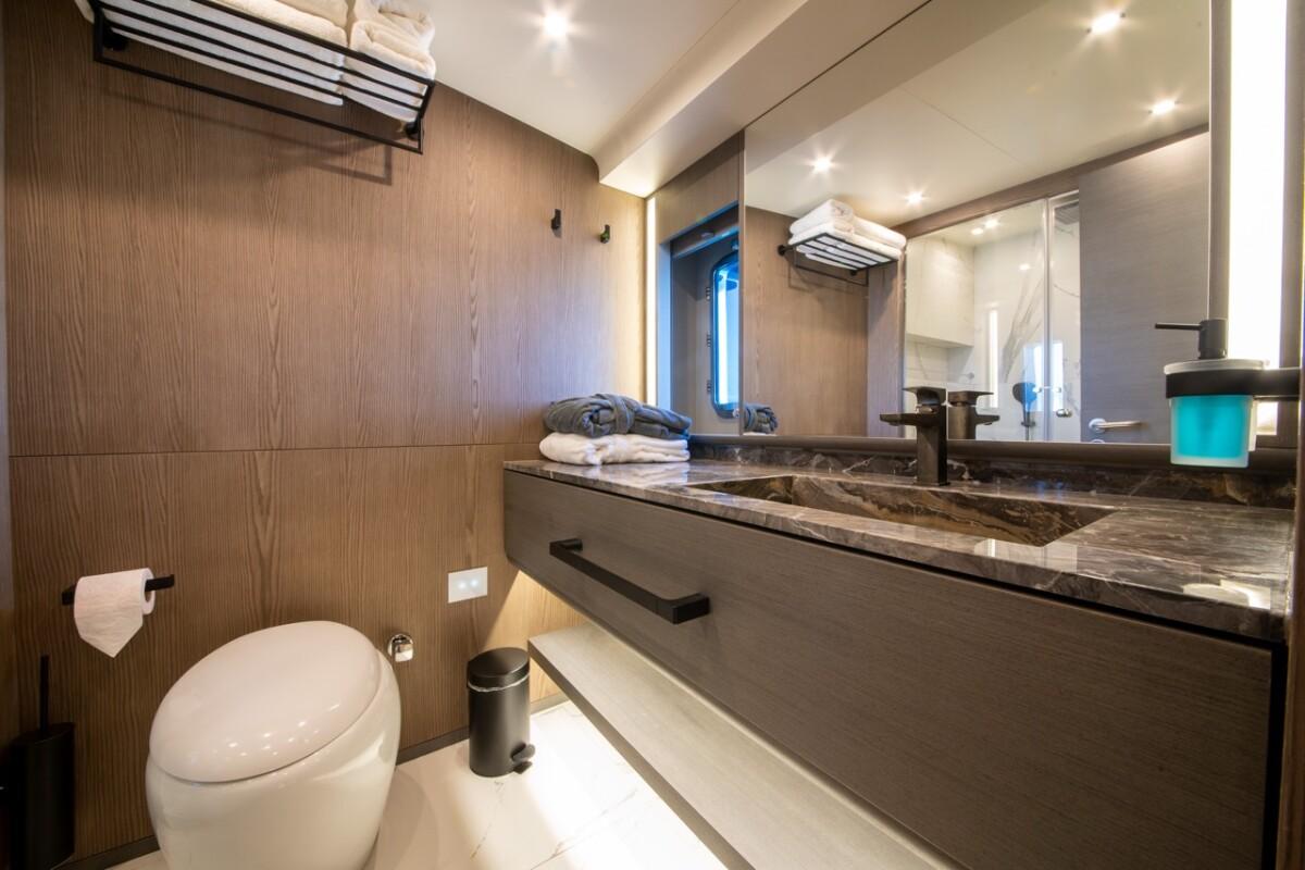 luxury yacht bathroom featuring dark marble vanity countertop, vessel sink, wall-mounted toilet, and wood paneling